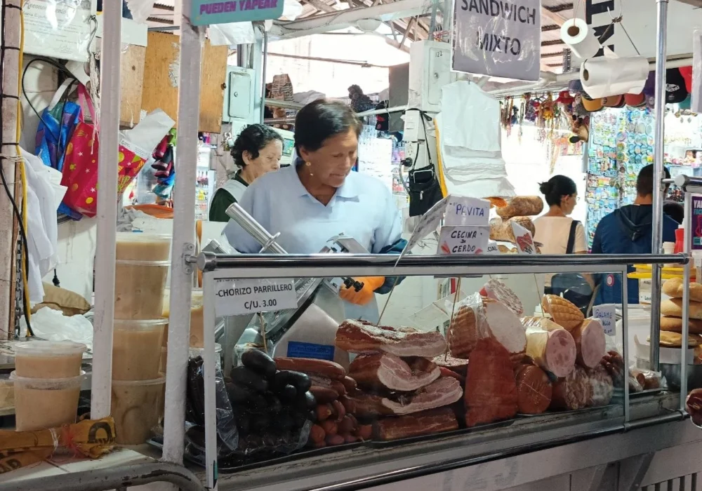Traditional food in Cusco at Mercado San Pedro: a vendor slicing cured pork at a sandwich stall
